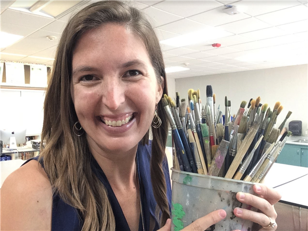 A smiling art teacher holding a cup full of paint brushes